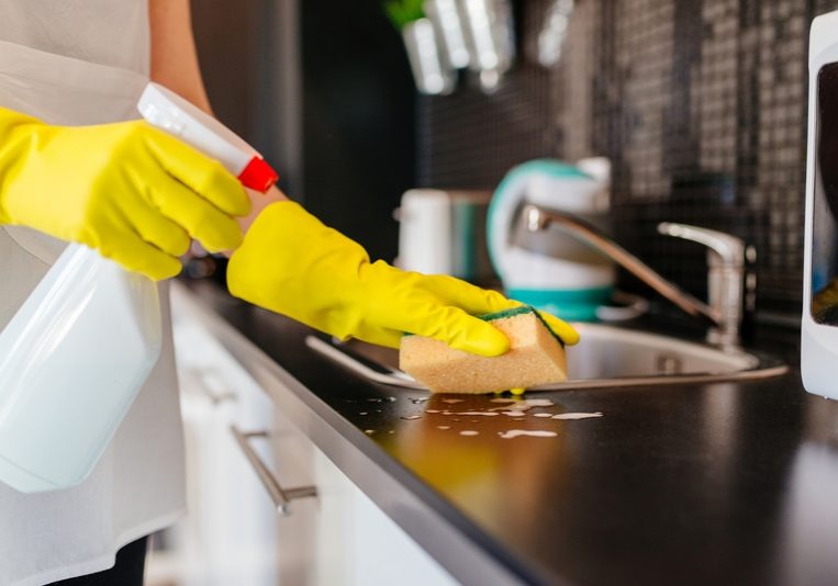 Woman cleaning kitchen cabinets with sponge